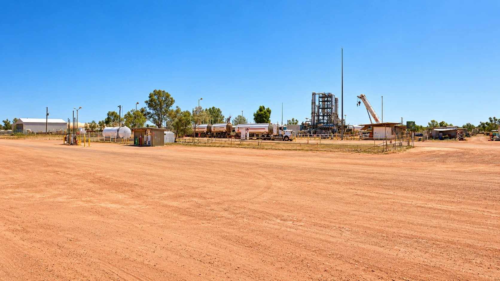 Remote oil field site on red dirt, with storage tanks, road tankers and a processing plant